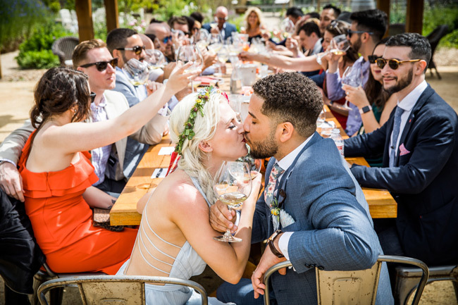 Newlyweds kiss at head of family-style wedding table | Budget-friendly wedding ideas