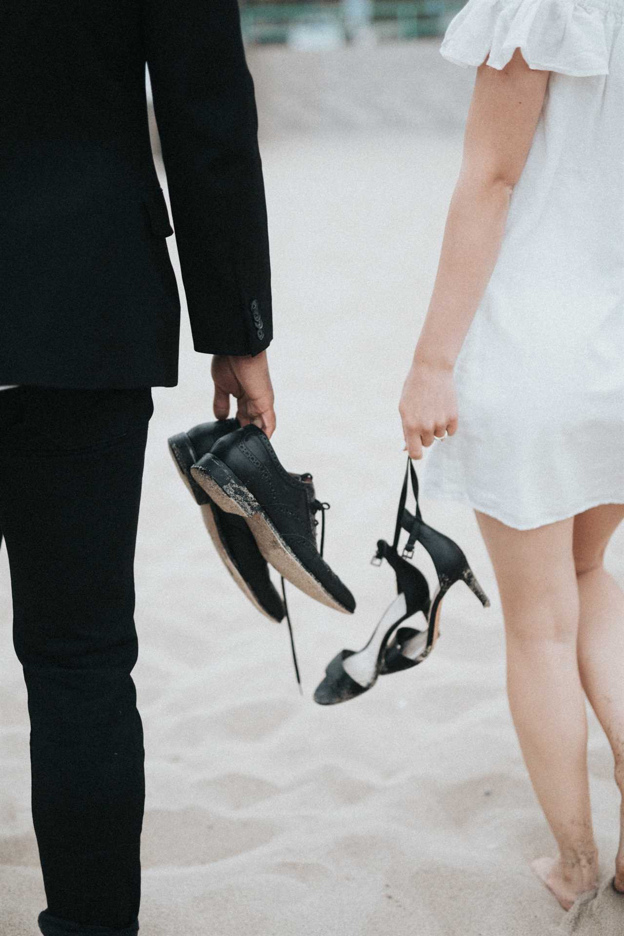 bride and groom walking on the beach with shoes in hand